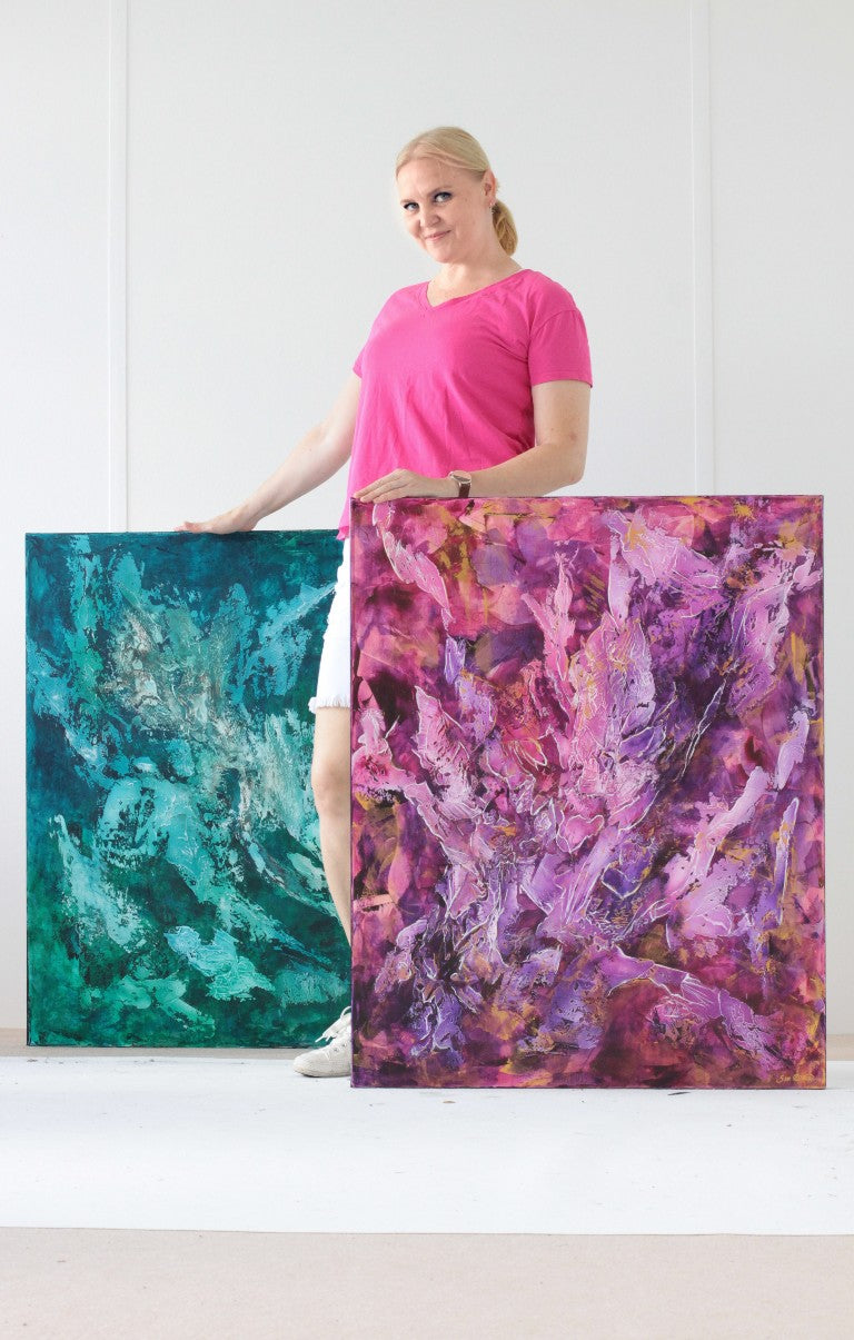 Female artist standing with two large abstract paintings.
